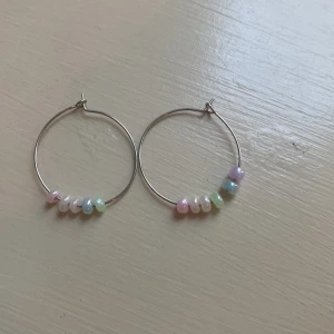Hoops med pastellfärgade pärlor - Säljer ett par stora hoops med pärlor i pastellfärger som rosa, blå, grön, lila och vitt. Örhängena är i tunn metall och har en enkel, stilren design med färgglada pärldetaljer som ger en lekfull touch.