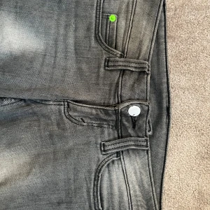 Grå bootcut jeans från Cheap Monday - Snygga grå jeans från Cheap Monday med bootcut passform och coolt slitna detaljer längs benen. Klassisk femficksmodell med silverfärgad knapp och grönt Cheap Monday-märke bak. Jeansen är i stretchigt denim och har en modern, lite urtvättad look.