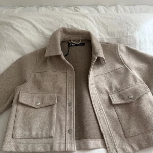Beige overshirt från Zara - Stilren beige overshirt från Zara med klassisk krage, stora fickor framtill med lock och tryckknappar. Den är för liten på mig hade annars haft på mig den så säljer den istället! 