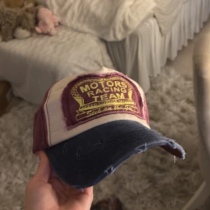 Motors Racing Team keps i vintage-stil - Cool keps med Motors Racing Team-tryck framtill. Kepsen har vinröda och vita paneler samt en mörkblå, lätt sliten skärm för en vintage look. Broderad patch i gult och vinrött ger extra attityd. Perfekt accessoar för dig som gillar streetwear och retro vibes.