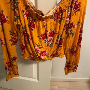 Gul blommig offshoulder blus H&M Divided - Superfin gul blus med röda och rosa blommor från H&M Divided. Offshoulder-modell med långa ärmar och smockdetaljer vid halsringning och midja. Luftig och lätt i bomull, perfekt för sommarens alla tillfällen. Snygg croppad passform.