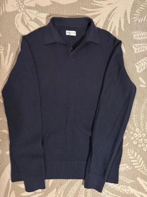 Mörkblå tröja från These Glory Days - Säljer en stilren mörkblå tröja från These Glory Days i storlek medium. Tröjan har krage, lång ärm och diskret strukturmönster i tyget. Perfekt för dig som gillar en klassisk look med modern twist.