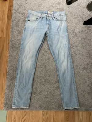 Ljusblå slim jeans - Säljer ett par ljusblå jeans med slim passform och klassisk femficksdesign. Jeansen har en snygg tvättad look och är tillverkade i denim. Perfekta för en avslappnad och trendig stil.