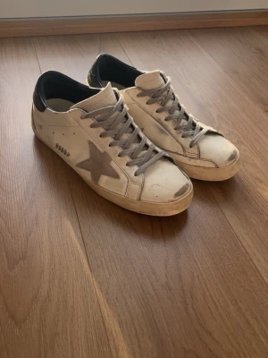 Golden Goose vita sneakers med grå stjärna - Säljer ett par vita Golden Goose sneakers med grå stjärna på sidan och gråa skosnören.  Storlek 44