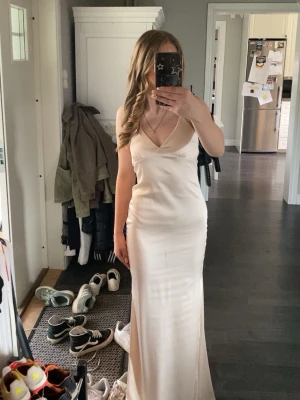 Champagnefärgad långklänning med smala axelband - Säljer min fina balklänning i champagnefärg med smala axelband och v-ringning. Klänningen har en figurnära passform och har snörning där bak. Känningen är i storlek 34 och kommer från Nelly. Ny pris var 899kr och säljer för 500kr💞
