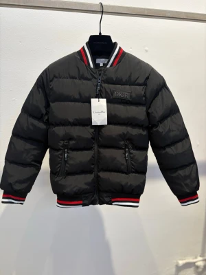 Dior Dunjacka (12-13Y) Kids  - Svart pufferjacka från Dior logga på bröstet. Jackan har dragkedja framtill, två fickor med dragkedja och ribbade muddar med röd, vit och svart rand vid ärmslut, krage och nederkant. Perfekt för kalla dagar.