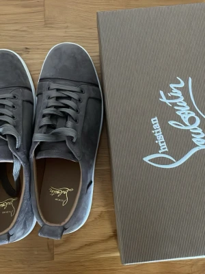 Gråa Christian Louboutin sneakers - Snygga gråa sneakers från Christian Louboutin i mocka med klassisk låg siluett och vita sulor. Skorna har matchande grå skosnören och diskret logga på insidan. Perfekta för dig som vill ha en stilren och exklusiv look. Passar storlek 43‼️‼️‼️‼️