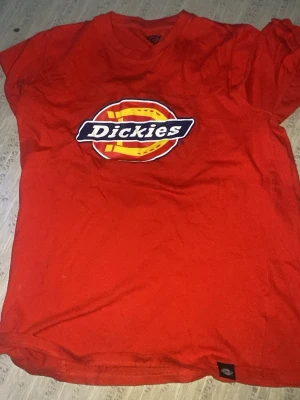 Röd Dickies t-shirt med logga - Snygg röd t-shirt från Dickies med stor tryckt logga på bröstet. Klassisk passform och rund halsringning, perfekt för en avslappnad streetstil. T-shirten är i bomull och har korta ärmar.