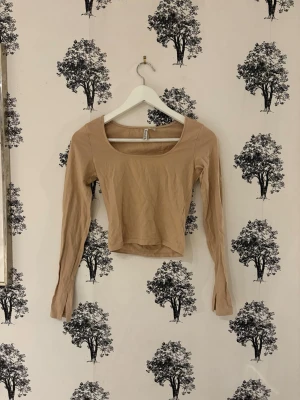 Beige croppad långärmad topp - Trendig beige croppad topp med lång ärm och bred, fyrkantig ringning. Perfekt att styla med höga jeans eller kjol. Mjuk och stretchig känsla, passar dig som gillar en enkel men snygg look.