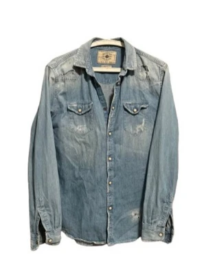 Ljusblå jeansskjorta med knappar - Snygg ljusblå jeansskjorta från Scotch & Soda med klassisk krage, bröstfickor med lock och tryckknappar. Skjortan har långa ärmar och är tillverkad i bomull. Perfekt för en avslappnad och trendig look.