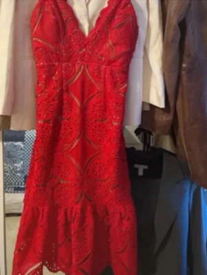 Röd spetsklänning med v-ringning - Snygg röd klänning med v-ringad hals och tunna axelband. Klänningen har ett detaljerat spetsmönster och volang nedtill. Perfekt för sommaren 