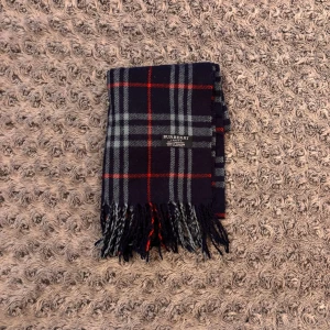 Burberry Halsduk - Snygg halsduk från Burberry i klassiskt rutigt mönster med mörkblå, grå och röda toner. Tillverkad i 100% kashmir för en lyxig och mjuk känsla. Tofsar i ändarna ger extra stilpoäng. Perfekt accessoar för att lyfta din outfit.
