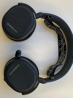 SteelSeries svarta gaminghörlurar - Säljer ett par svarta Steelseries Arctis 5 gaminghörlurar med RGB samt mjuka öronkuddar och justerbart huvudband. Hörlurarna har en infällbar och utfällbar mikrofon. OBS. Se bilder att sladden har lite skador på sig, men funkar att använda bara plastskalet som har gått av. 