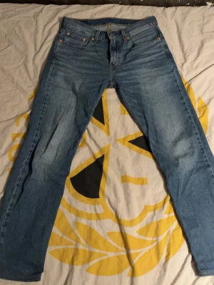 Levi's blå raka jeans - Klassiska blå jeans från Levi's med rak passform och fem fickor. Jeansen har en ljus tvätt och den ikoniska röda Levi's-lappen på bakfickan samt läderpatch i midjan. Tillverkade i slitstark denim, perfekta för en avslappnad och tidlös stil.