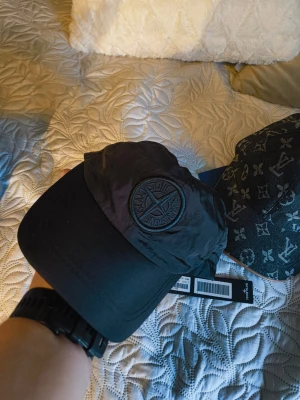 Svart keps från Stone - Snygg svart keps från Stone  med klassisk böjd skärm och broderad logotyp framtill. Tillverkad i lätt och slitstarkt material med justerbar rem bak. Perfekt för dig som vill ha en stilren och trendig accessoar.