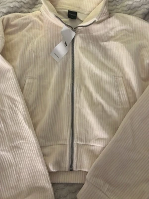 beige vit ziphoodie från Topten - Snygg vit ziphoodie från Topten med två sidofickor. Hoodie har en klassisk krage och är tillverkad i ett mjukt, ribbat tyg som ger en retrovibe. Perfekt för dig som gillar stilrena och bekväma plagg. Är ifrån Sydkorea och har bara legat i garderoben utan användning. Passar mig som har xxs-xs