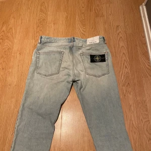 Ljusblå jeans från Stone Island - Säljer ett par ljusblå jeans från Stone Island med klassisk femficksmodell och ikonisk svart patch med logga på bakfickan. Jeansen har raka ben och är tillverkade i ett mjukt denimtyg. Perfekta för en avslappnad och trendig stil.