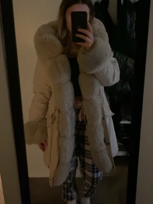 Beige pälsjacka med fluffig krage - Säljer en beige pälsjacka med stor, fluffig fuskpäls längs krage, ärmslut och framkant. Jackan har dragsko i midjan och stora fickor framtill. Den har lite fläckar men inget man tänker på mycket, kan skicka bild om man vill se ❤️