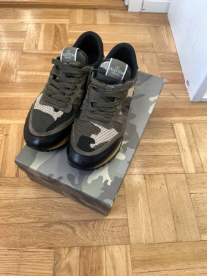 Valentino rockrunners garavani - Snygga sneakers från Valentino med militärgrönt camo-mönster, svarta detaljer och robust sula. Skorna har lågt skaft och är tillverkade i en mix av textil och läder. Perfekta för dig som gillar streetstyle och exklusiva märken.