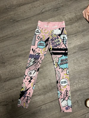 Färgglada leggings från stronger -  leggings från STRONGER med serietidningsinspirerat tryck i rosa, blått, svart och gult. Hög midja och tight passform.