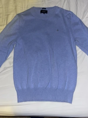 Ljusblå tröja från Boomerang - Ljusblå stickad tröja från Boomerang med rund halsringning och diskret broderad logga på bröstet. Tröjan har ribbade muddar vid ärmslut och nederkant. Perfekt för lager-på-lager och enkel att matcha med jeans