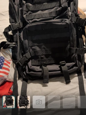 Svart taktisk ryggsäck med många fack - Produktegenskaper: Design: Militärinspirerad design med flera fack och yttre kompressionsremmar. Fästsystem: Ryggsäcken är utrustad med MOLLE/PALS-kompatibla band (Modular Lightweight Load-carrying Equipment / Pouch u Ladder System) på framsidan och sidorna, vilket möjliggör anpassning med extra fickor och utrustning. Material: Ofta tillverkade av slitstarka material som polyester med vattenavvisande beläggning. Användning: Populär för friluftsliv, prepping, jakt och vardagsbruk.