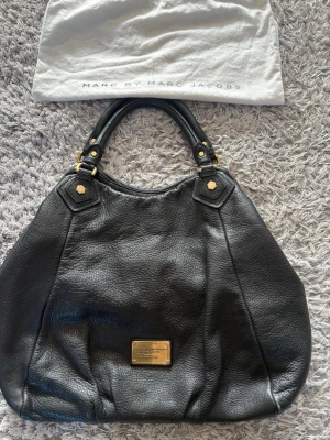 Svart handväska från Marc by Marc Jacobs - Säljer nu min svarta handväska i skinn från Marc by Marc Jacobs med guldfärgade metalldetaljer och dubbla handtag. Den är i mycket bra skick, hör av er vid frågor eller funderingar!