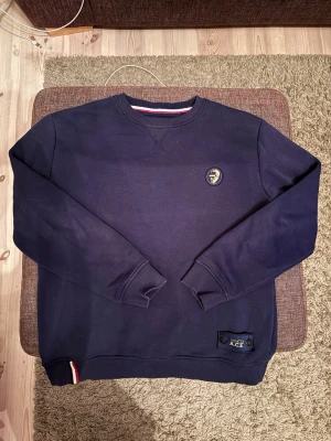 Mörkblå sweatshirt från North Sails - Mörkblå sweatshirt från WHO’s A.C.E med rund halsringning och ribbade muddar. Liten logotyp på bröstet och snygg detalj med röd, vit och blå rand vid nederkanten. Perfekt för en avslappnad stil. Den passar dig som är runt 170-175 cm lång.