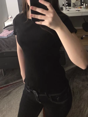 Svart ribbad t-shirt från Lindex - En svart ribbad t-shirt från Lindex med rund halsringning och korta ärmar. T-shirten har en slim passform och är tillverkad i mjuk bomull, perfekt för en stilren och enkel look.