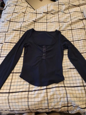 Mörkblå ribbad topp med knappar - Snygg mörkblå kroppad långärmad topp. Toppen har en fyrkantig ringning och är figurnära i modellen. Använd endast ett antal gånger men säljer då jag inte gillar när den är kroppad.
