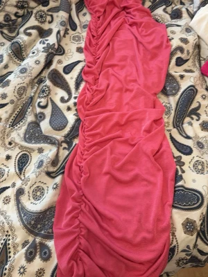 Rosa omlottklänning med rynk - Trendig rosa klänning med omlott och rynkade detaljer längs hela längden. Klänningen har en figurnära passform och är tillverkad i ett mjukt, stretchigt material som ger en snygg siluett. Perfekt för dig som vill sticka ut med färg och form.