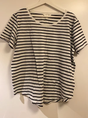 Randig vit och svart t-shirt - En klassisk vit t-shirt med svarta horisontella ränder och rund hals. T-shirten har korta ärmar och är tillverkad i mjuk bomull, perfekt för en avslappnad och enkel stil.