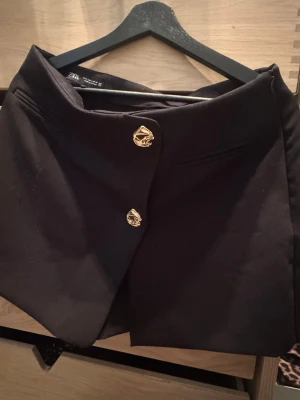 Svart skort från Zara med guldknappar - Stilren svart skort från Zara med snygga guldfärgade knappar framtill. De är skjorts under! Knappt använd! Dm för fler bilder!💛