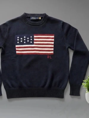 Mörkblå stickad tröja Ralph Lauren - Mörkblå stickad tröja från Ralph Lauren med stor amerikansk flagga på bröstet och RL-broderi. Tröjan har rund halsringning och ribbade muddar vid ärmslut och nederkant. Perfekt för dig som gillar klassisk preppy stil.