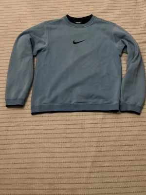 Ljusblå Nike sweatshirt - Säljer en ljusblå vintage sweatshirt från Nike med klassisk svart swoosh-logga på bröstet. Tröjan har rund halsringning, långa ärmar och är gjord i mjukt material. Perfekt för en avslappnad och sportig stil. Pris kan diskuteras.