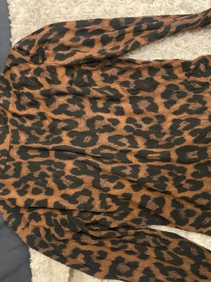 Leopardmönstrad blus med långa ärmar - Snygg blus med leopardmönster i brunt och svart. Blusen har långa ärmar och en rak passform. Perfekt för dig som vill sticka ut med ett djurmönstrat plagg. Materialet känns lätt och följsamt mot kroppen.