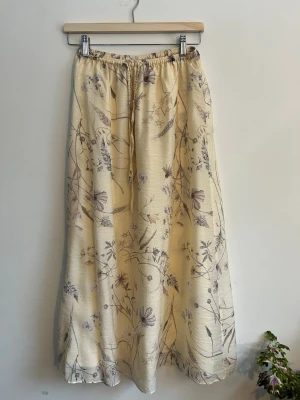 Blommig beige kjol från H&M XS - Fin beige kjol från H&M i storlek XS med blommigt mönster i lila och grå toner. Kjolen har resår i midjan och är i ett mjukt, lätt tyg som faller snyggt. Perfekt för en avslappnad och trendig look. Använd en gång jättefint skick. Stor i storlek kan passa M.