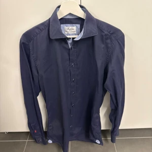 Mörkblå skjorta från Stenströms - Klassisk mörkblå skjorta från Stenströms med lång ärm och knappar framtill. Skjortan har en stilren krage och diskreta detaljer vid manschetterna. Perfekt för en clean och snygg look.