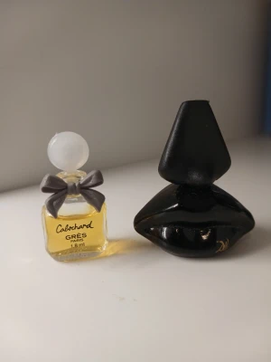 Cabochard Gres miniparfym & svart vintageparfym 1973🌻🌹 - Säljer en söt miniparfym Cabochard Gres Paris 1,8 ml i glasflaska med rund vit kork och grå rosett, samt en unik svart parfymflaska formad som läppar med konisk kork. Perfekt för dig som gillar snygga och annorlunda parfymflaskor.💕