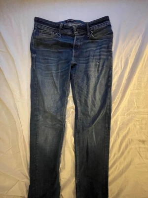 Mörkblå jeans från Jack & Jones - Snygga mörkblå jeans från Jack & Jones med klassisk femficksdesign och raka ben. Jeansen har diskreta slitningar och en läderpatch med logga bak i midjan. Perfekta för en avslappnad och trendig look.