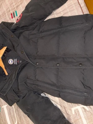 Svart Canada Goose Wyndham - Säljer en svart dunjacka Canada Goose Wyndham i storlek S. Jackan har inga skador. Inga hål. Möjligen endast små spår av vanlig användning. Kommer med äkta pläls till luvan (tagit bort den i bilderna). Självklart äkta. Kan fixa mer bilder vid intresse. Köpt på miinto, över 3 år sen. Fraktas.