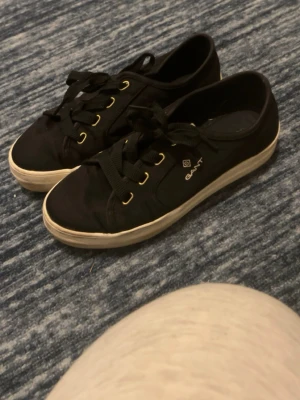 Svarta låga sneakers från Gant - Svarta sneakers från Gant med vita sulor och svarta skosnören. Skorna har guldfärgade öljetter och Gant-logga på sidan. Klassisk låg modell med rund tå och canvasmaterial . Inte använda mycket men lite då de som syns på bilderna men de går säkert att tvätta bort🫶🏼det står ingen storlek i dom men jag tror dom är 38💕