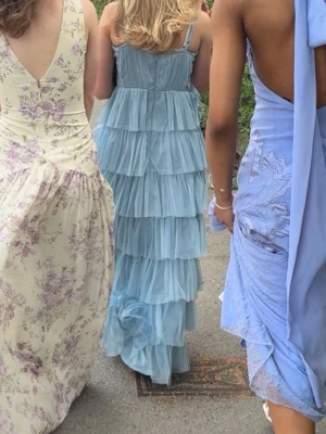 Ljusblå balklänning - Säljer en lång, ljusblå balklänning med flera lager volanger och smala axelband. Klänningen har v-ringad urringning och är tillverkad i ett lätt, luftigt material. Perfekt för skolbal eller bröllop. Jag på bilderna är ca 155-157cm. Och passar någon runt den längden. Den har justerbara band och en dragkedja ända ner till svanken. Superfin och skön!💙