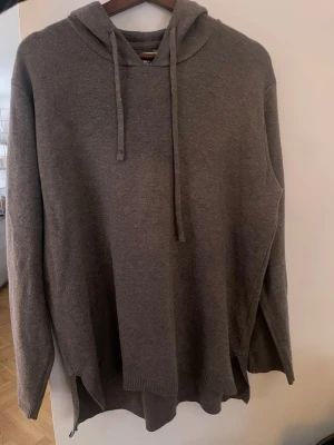 Brun stickad hoodie med huva - Mysig brun stickad hoodie med huva och dragsko. Långärmad modell med avslappnad passform och ribbade muddar. Perfekt för dig som gillar en enkel och stilren look. Materialet känns mjukt och skönt mot huden. Skulle säga M/L i storlek