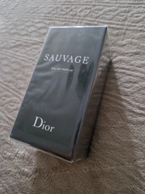 Dior Sauvage Eau de Parfum - Dior Sauvage Eau de Parfum i elegant svart förpackning med vit text. Flaskan är troligtvis av glas och parfymen är känd för sin fräscha och maskulina doft. Perfekt för dig som vill ha en ikonisk och modern parfym från ett lyxigt märke.