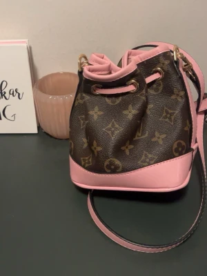 Louis Vuitton Monogram axelväska rosa - Snygg axelväska från Louis Vuitton i klassiskt monogrammönster med detaljer i ljusrosa läder. Väskan har dragskostängning, justerbar axelrem och guldfärgade metalldetaljer. Perfekt för dig som vill ha en trendig och lyxig accessoar.