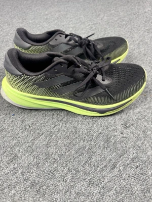 Adidas Supernova svarta/lime sneakers - Snygga Adidas Supernova sneakers i svart mesh med limegröna detaljer och sula. Skorna har klassiska tre ränder på sidan, snörning och låg profil. Perfekta för dig som gillar sportig stil och vill ha lätta, ventilerande sneakers.