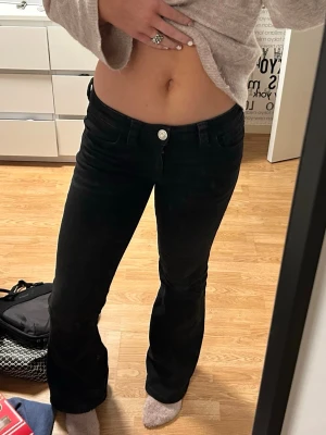 Svarta low waist bootcut jeans - Säljer ett par svarta low waist jeans med bootcut-modell och vita kontrastsömmar baktill. Jeansen är knappt använda!