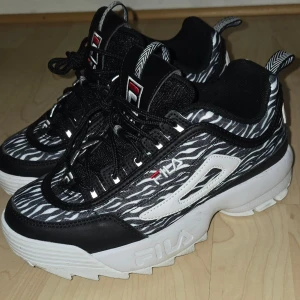 Fila Disruptor sneakers zebra-mönster - Snygga Fila Disruptor sneakers med svartvitt zebramönster, chunky vit sula och svarta detaljer. Skorna har Fila-logga på sidan samt svarta skosnören. 