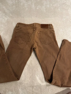 Bruna jeans från Jacob Cohen W-33 L-32.      6 - Snygga bruna jeans från Jacob Cohen med klassisk femficksdesign och knappgylf. Jeansen har en rak passform och är tillverkade i mjuk bomull med exklusiv känsla. Perfekta för dig som gillar stilrena och tidlösa byxor med italiensk touch.